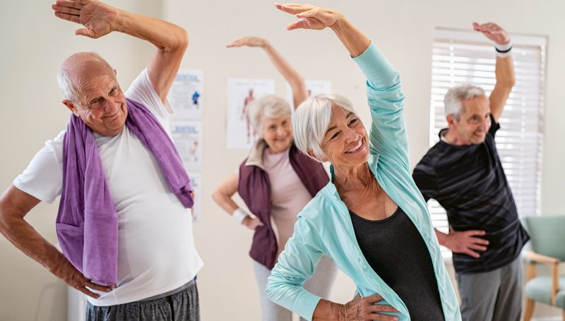 Group,Of,Seniors,Doing,Stretching,Exercise,Together,At,Retirement,Centre.